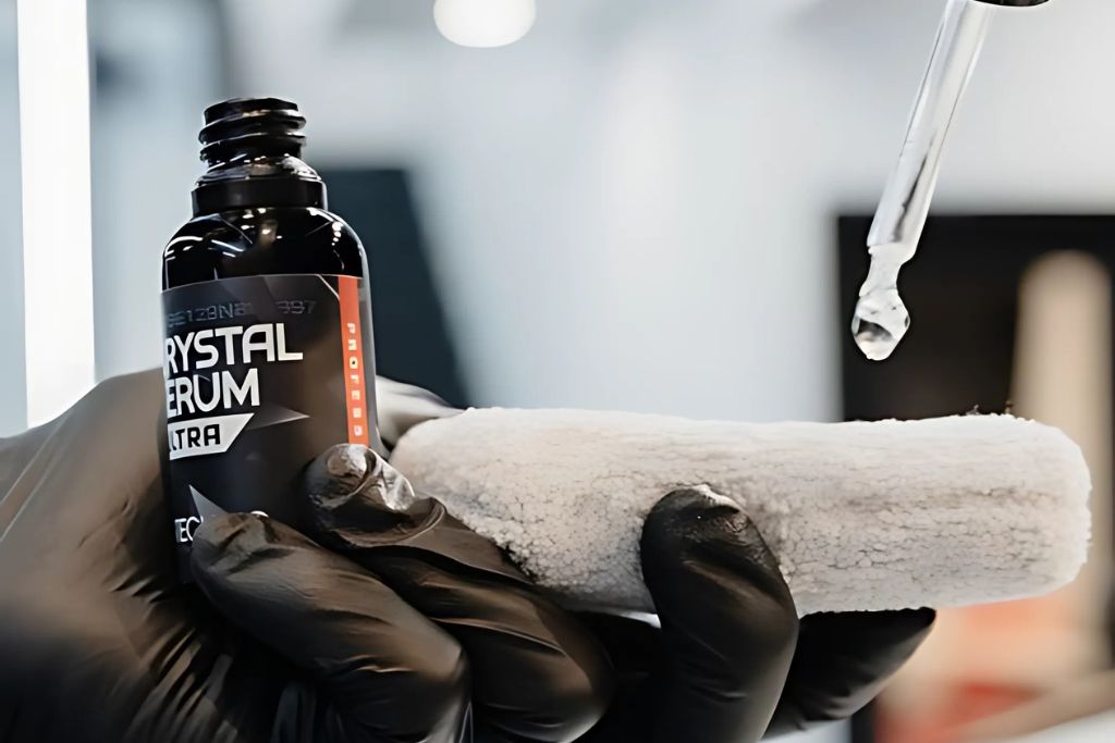 A close-up of Gtechniq Crystal Serum Ultra being applied with precision, as a drop of the coating drips from a dropper onto a microfiber applicator held by a gloved hand.