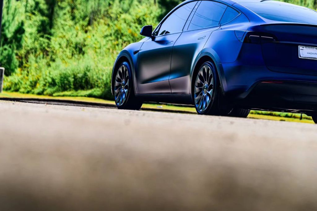 A sleek, dark-blue Tesla with a matte finish parked outdoors on a sunny day, showcasing its ceramic-coated exterior reflecting minimal light.