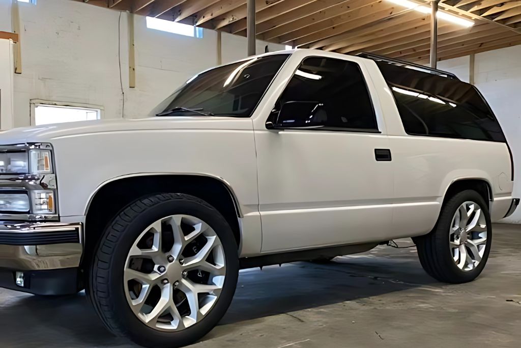 A customized white SUV with dark-tinted windows and large chrome wheels parked inside a detailing shop, showcasing the stylish and protective benefits of professional automotive window tinting.