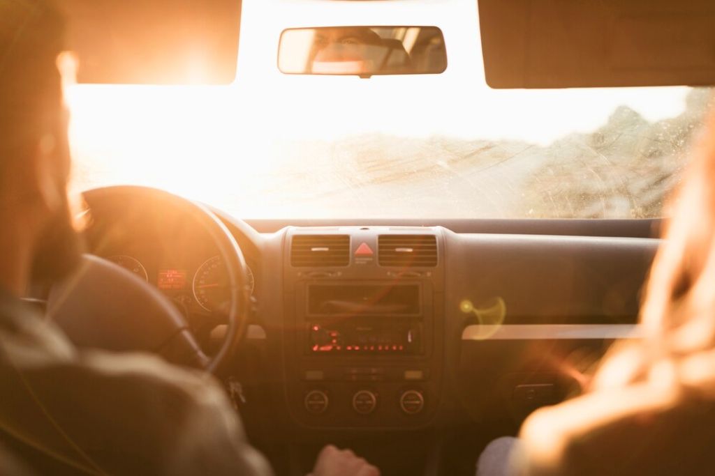Two people driving into the intense sunlight with glare visibly affecting the windshield, illustrating the need for window tinting to improve driving comfort and visibility.