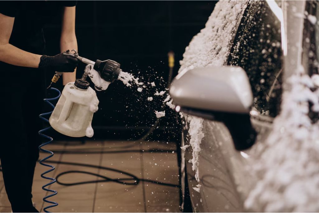 A person uses a foam cannon to spray thick white foam onto a car during a hand wash, emphasizing a gentle and controlled cleaning method for vehicles with ceramic coating.