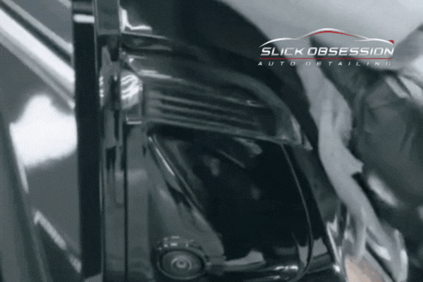 A close-up animation of a professional detailer in gloves gently applying ceramic coating to the edge of a glossy black vehicle using a microfiber applicator pad. The "Slick Obsession Auto Detailing" logo appears in the corner, reinforcing the branding.