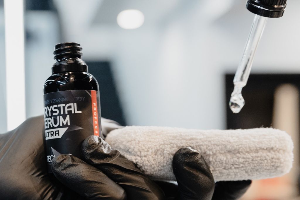 Close-up of ceramic coating liquid being carefully applied to a soft microfiber cloth, visually demonstrating how ceramic coating helps prevent scratches by creating a protective layer.