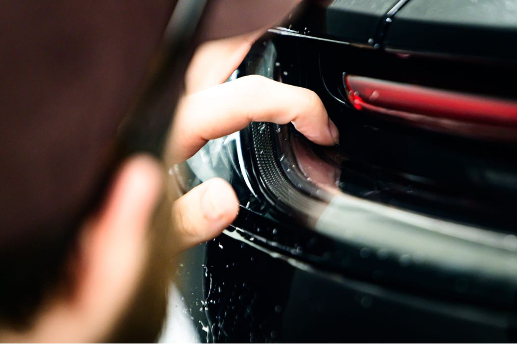 Close-up of a person carefully inspecting the front bumper of a car for imperfections or chips, highlighting what ceramic coating cannot do, such as fully preventing rock chips or heavy impact damage.