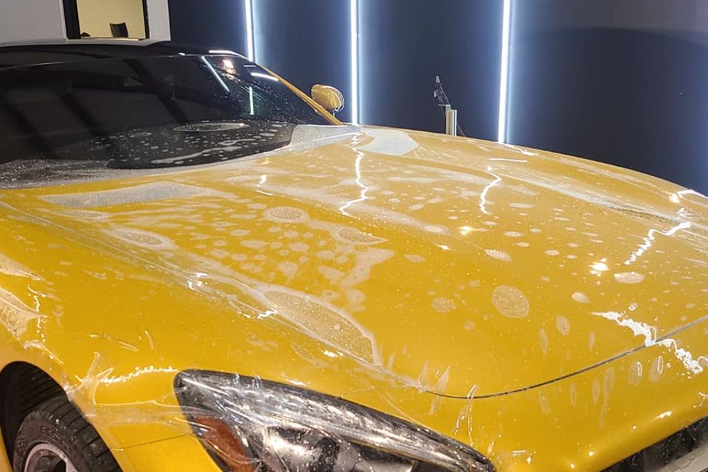 A yellow sports car undergoing Paint Protection Film installation, with the transparent film partially applied and water bubbles visible across the hood. This close-up showcases how PPF is carefully fitted to shield the vehicle from Birmingham’s harsh elements like bird droppings, UV rays, and tree sap.