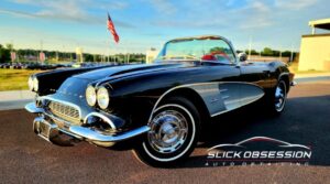 Shiny black classic Corvette with whitewall tires parked under clear fall skies in Birmingham, AL, showcasing a flawless paint job protected by PPF, with the Slick Obsession Auto Detailing logo in the corner.