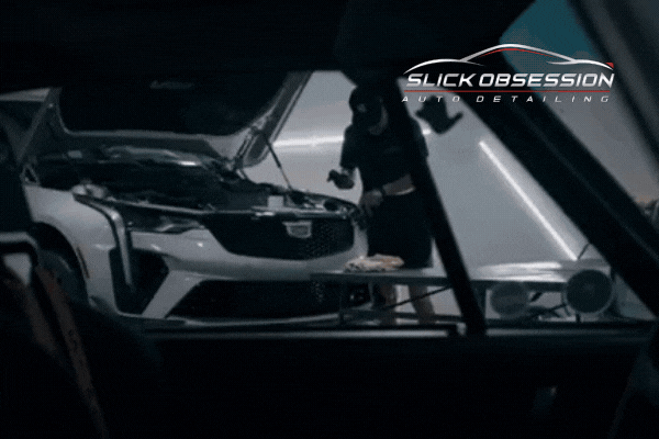 A detail technician at Slick Obsession works on a white luxury car in a clean, well-lit garage, applying paint protection film with precision tools. The scene highlights the importance of expert PPF installation to withstand Birmingham’s unpredictable fall moisture and humidity.