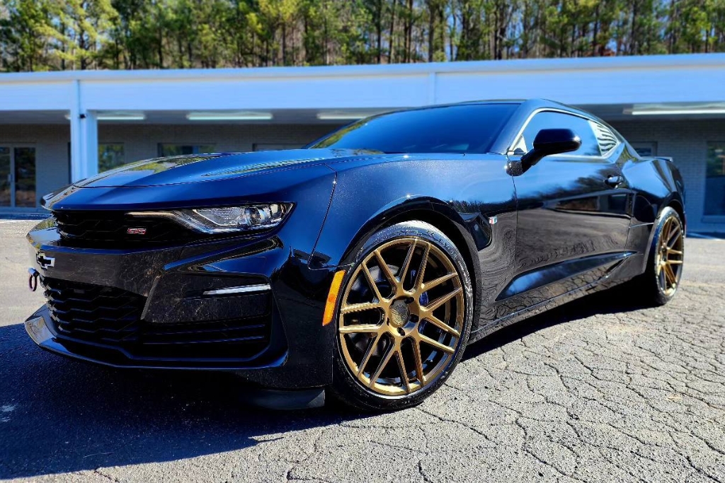 Glossy black Chevrolet Camaro with bronze wheels parked in front of Slick Obsession Auto Detailing in Birmingham AL. The vehicle's mirror-like finish reflects the long-lasting results of a professional ceramic coating, supporting the question how long does ceramic coating last.