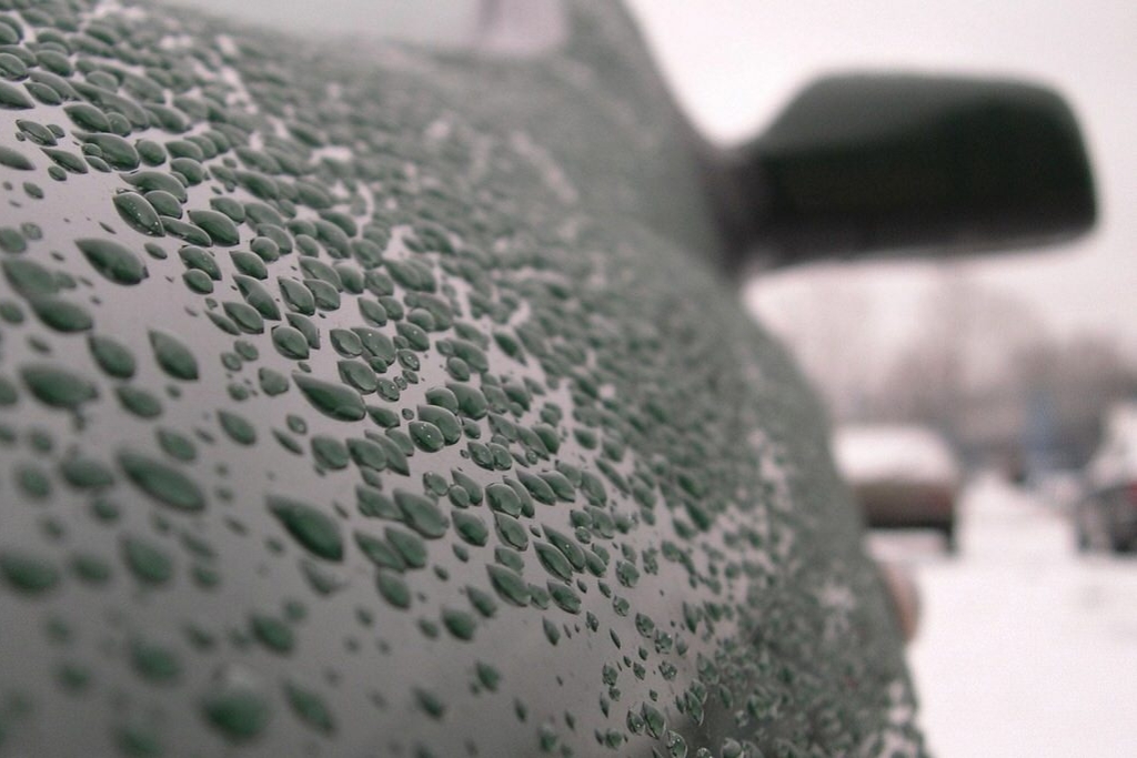 Close-up of water beading on a ceramic-coated dark green car panel during winter, visually highlighting the hydrophobic and protective qualities of the coating. Captured in a snowy environment, this image supports the topic Benefits of Ceramic Coating as offered by Slick Obsession Auto Detailing in Birmingham, AL.