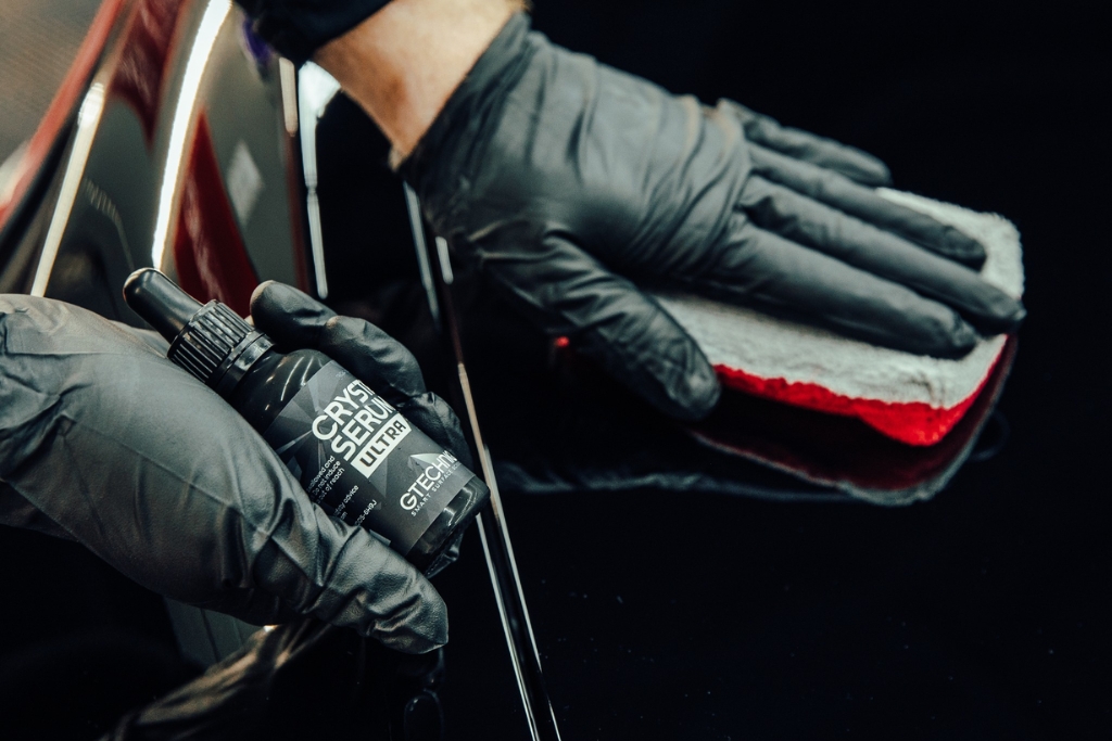 Close-up of a technician at Slick Obsession Auto Detailing in Birmingham AL applying Gtechniq Crystal Serum Ultra ceramic coating to a black vehicle surface using an applicator pad. This premium product contributes to Ceramic Coating Cost and long-term protection.