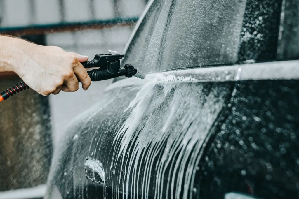 Close-up of a hand using a foam cannon to apply soap during a hand wash on a black vehicle. The foamy surface illustrates proper care techniques as part of maintenance tips after ceramic coating.