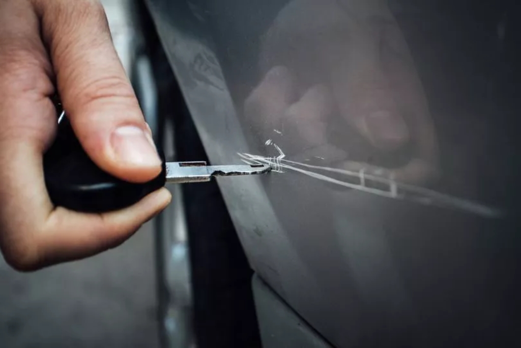 A close-up of a hand scratching a gray car door with a key, showing visible paint damage to emphasize that even high-quality coatings from Slick Obsession in Birmingham, AL have limits. This image illustrates a key point in the discussion of what Ceramic Coating can't do.