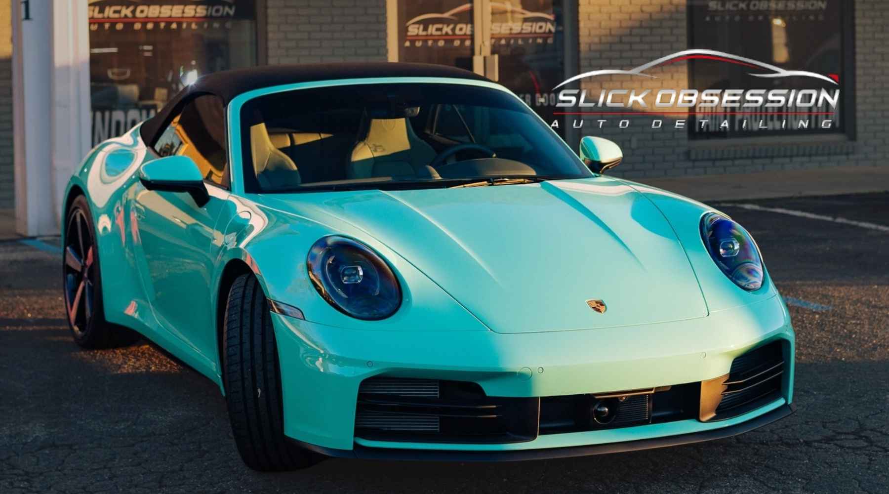 A glossy turquoise Porsche with a black convertible top parked outside Slick Obsession Auto Detailing in Birmingham AL. The car’s reflective finish highlights the results of a professional ceramic coating job, emphasizing ceramic coating cost and quality service.