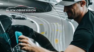 Detailing technician from Slick Obsession Auto Detailing in Birmingham, AL smooths out paint protection film on a vehicle's glossy surface, showcasing the process in action for those asking what is paint protection film.