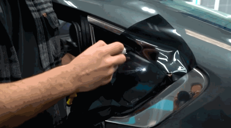 Close up of a technician heat shaping Ceramic Window Tint film over a car headlight to ensure a precise fit before final installation.