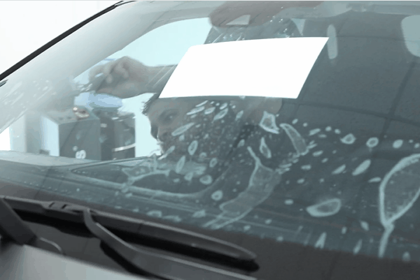 Technician carefully installing window tint film on a vehicle windshield inside a professional auto detailing facility. The image highlights expert window tint installation in Birmingham to ensure proper heat rejection, seamless edges, and long term performance in extreme summer temperatures.