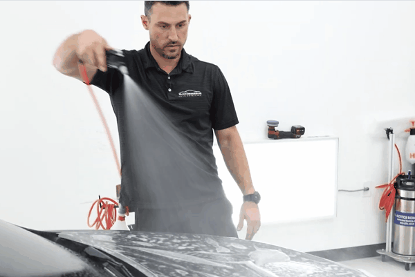 Professional technician spraying slip solution onto a vehicle hood during paint protection film installation inside a clean detailing facility. The image highlights the importance of professional PPF installation in Birmingham AL, showing controlled application techniques that prevent lifting edges and trapped debris.